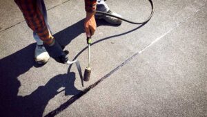 Person using a soft roof rake to clear leaves from a low-slope shingle roof.