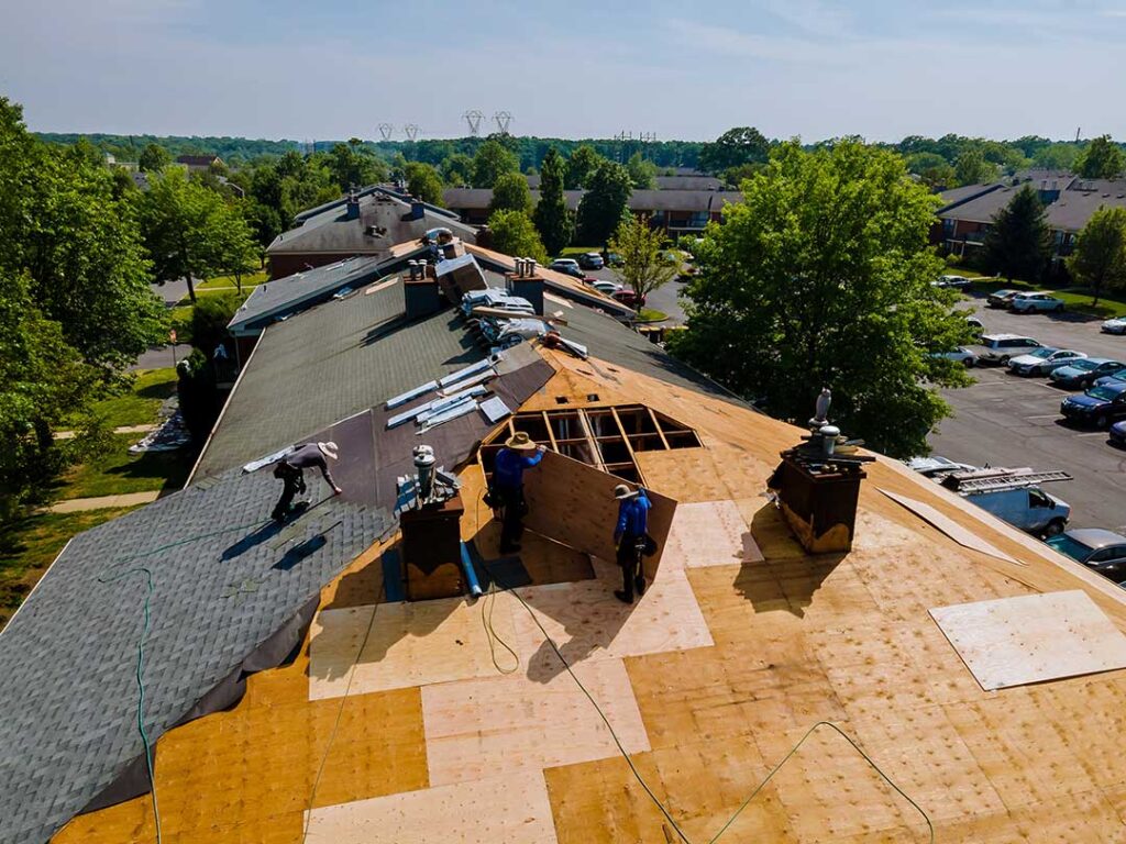A homeowner examines a ceiling water stain beneath a roof leak while a bucket catches dripping water.