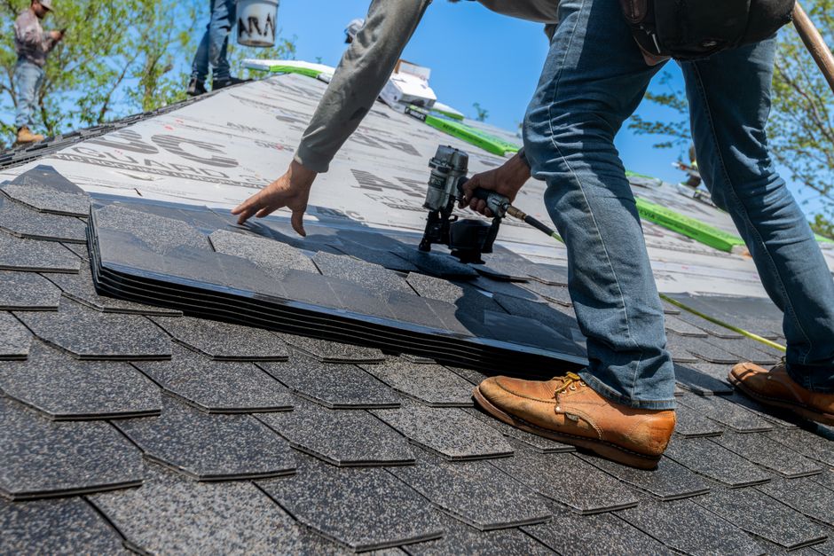 A roof worker examines exposed decking beside old shingles during a residential roof inspection.