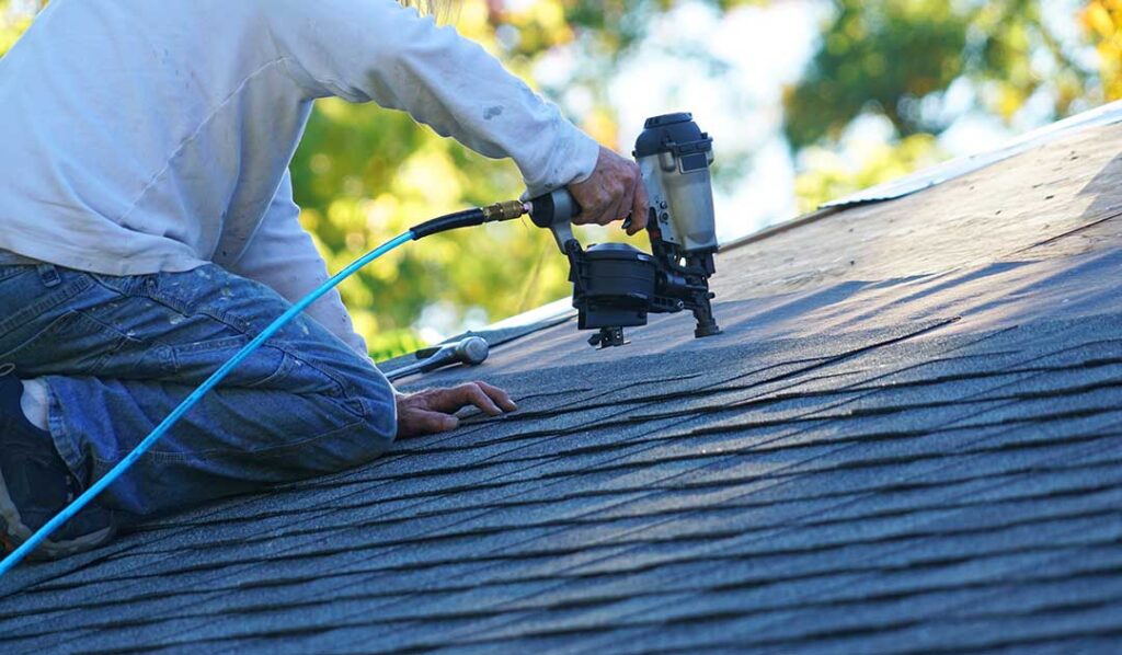 Close view of bruised asphalt shingles with missing granules beside a dented metal gutter after a hailstorm.